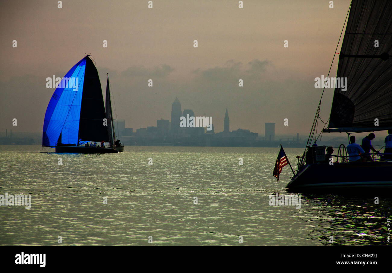 two sailboats in front of  the misty outline of Cleveland, Ohio - sunlight thru blue spinaker and american flag Stock Photo
