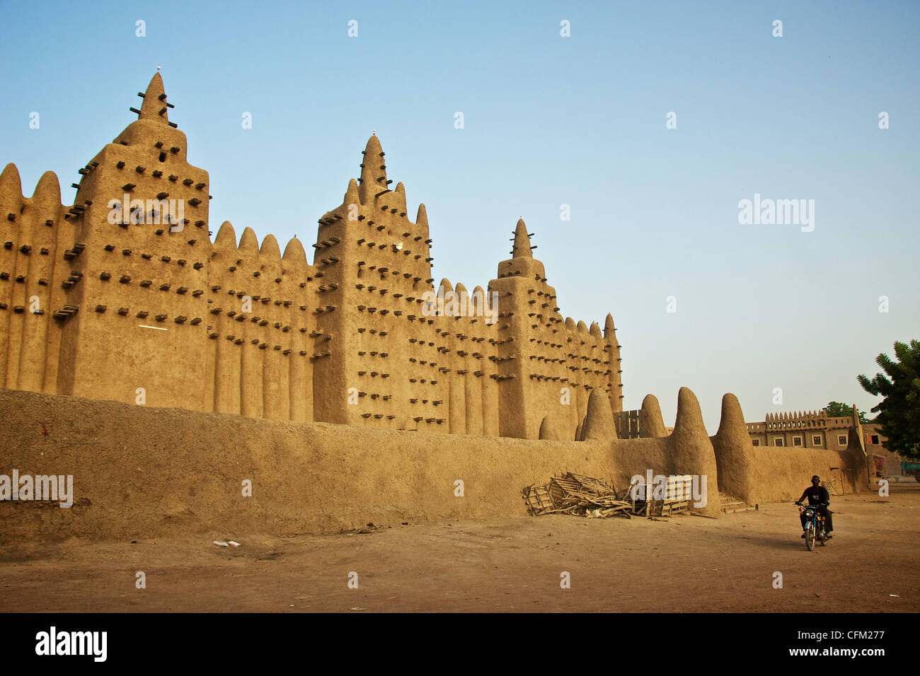 A man rides his motorbike by the Great Mosque of Djenne in Djenne, Mali. Stock Photo