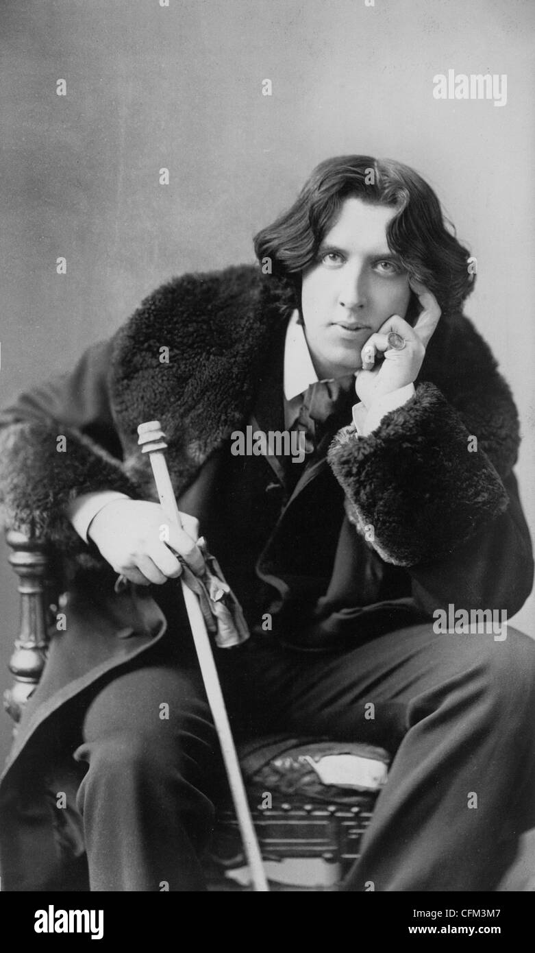 Oscar Wilde, leaning forward, left elbow resting on knee, hand to chin, holding walking stick in right hand, wearing coat, circa 1882 Stock Photo