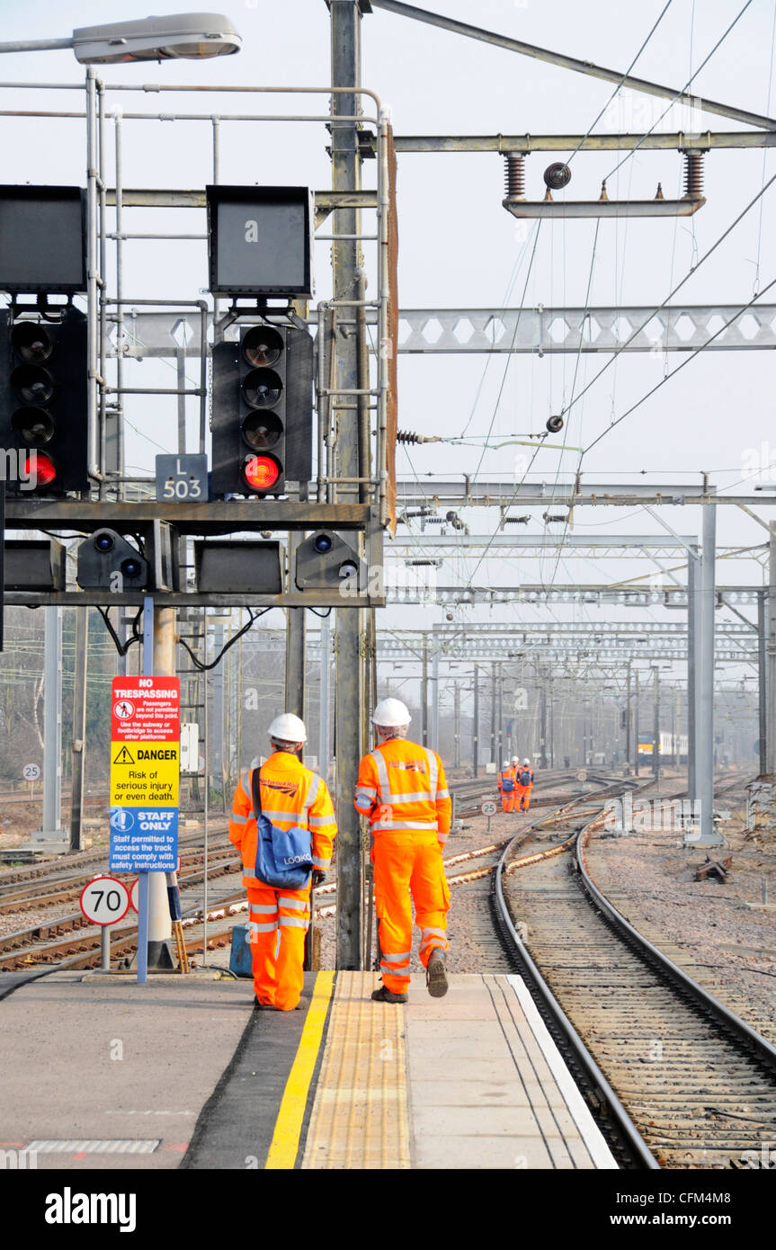 Back view Network Rail workmen in high vis jacket & hard hat at railway signal sign group of workers on tracks beyond train distant Essex England UK Stock Photo