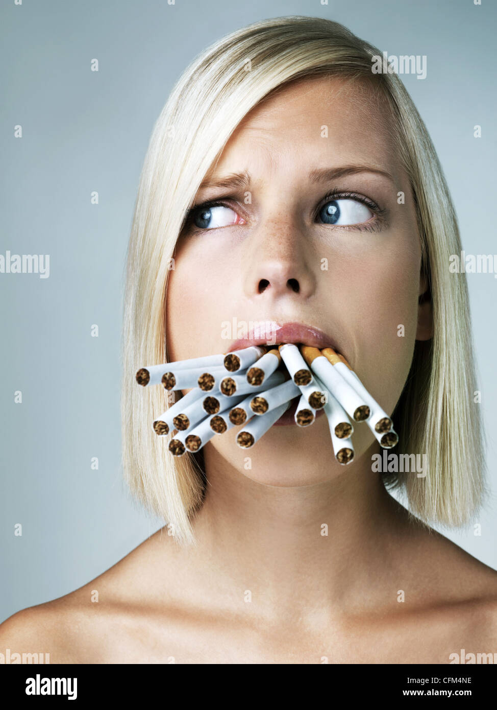 Studio portrait of young woman with mouthful of cigarettes Stock Photo