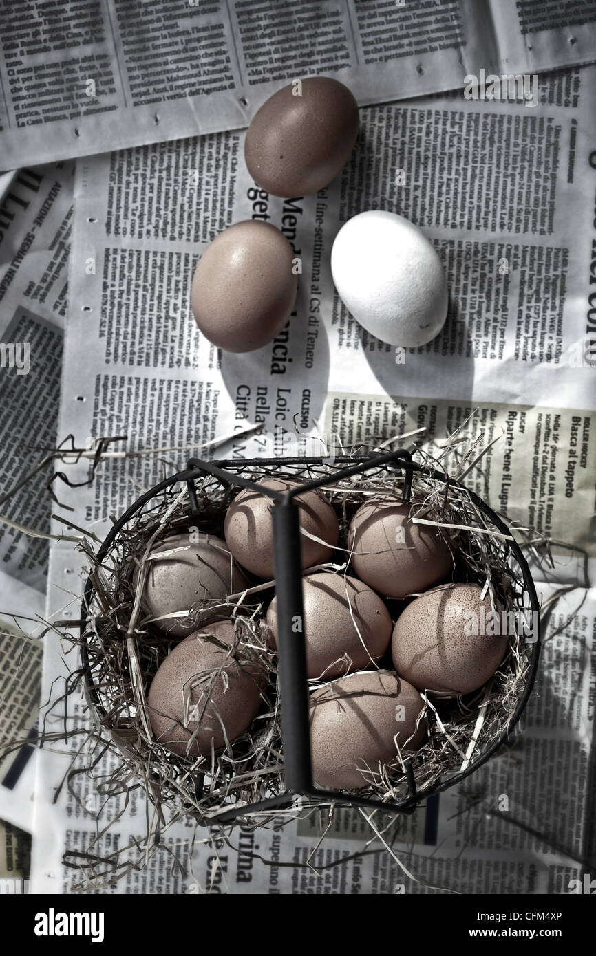 Eggs in a basket with straw on newsprint Stock Photo