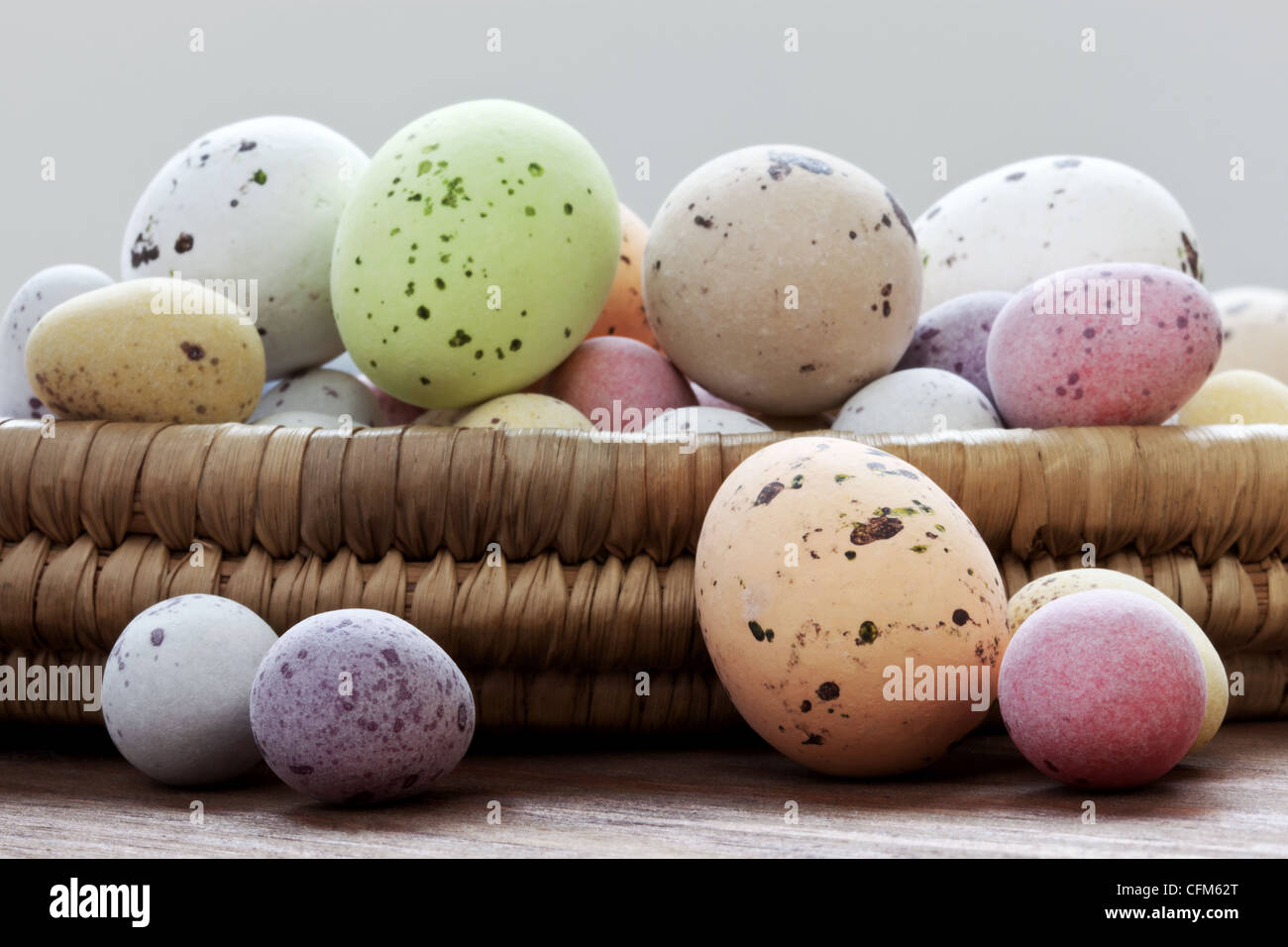 Still life photo of speckled candy covered chocolate easter eggs in a wicker basket on a rustic wooden table. Stock Photo