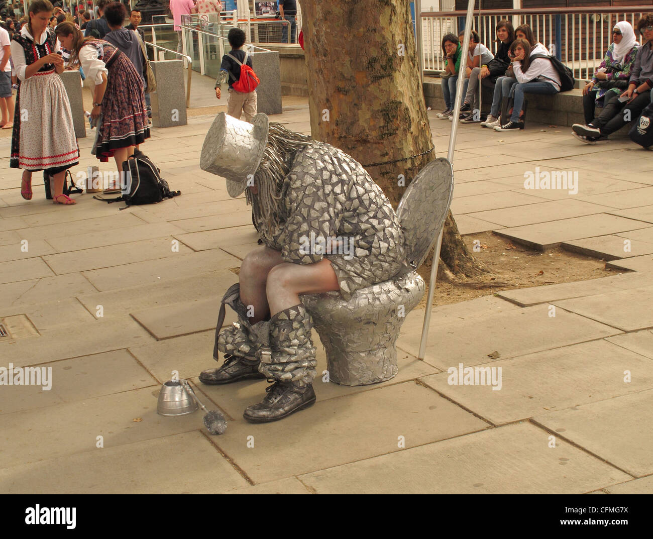 Silver coloured street performer on the SouthBank in London sitting on pretend toilet Stock Photo