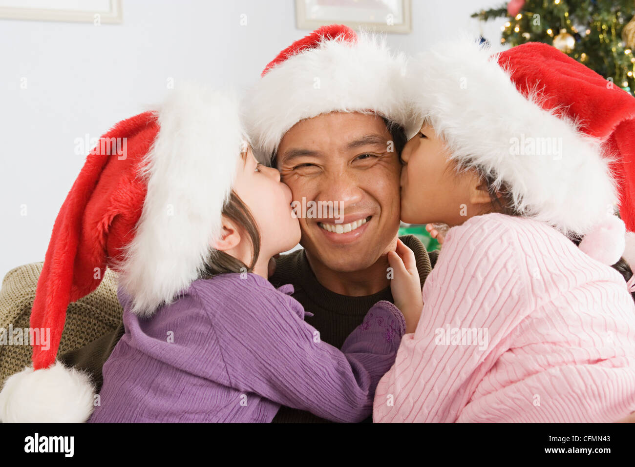 USA, California, Los Angeles, daughters (10-11) kissing father wearing santa hat Stock Photo