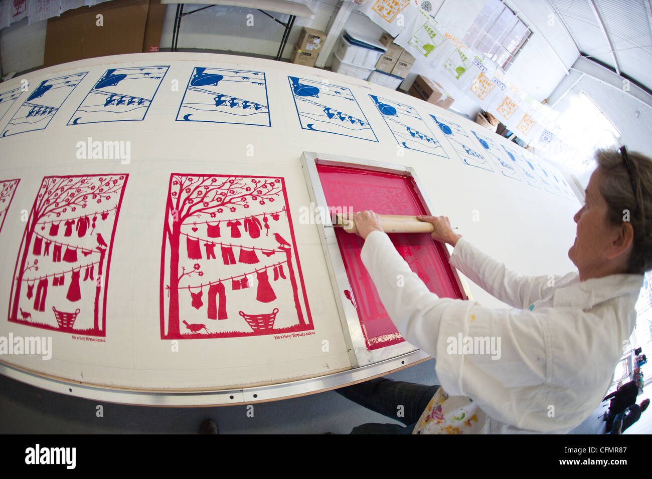 A woman silkscreens original design on to cotton fabric in artist's studio. Stock Photo