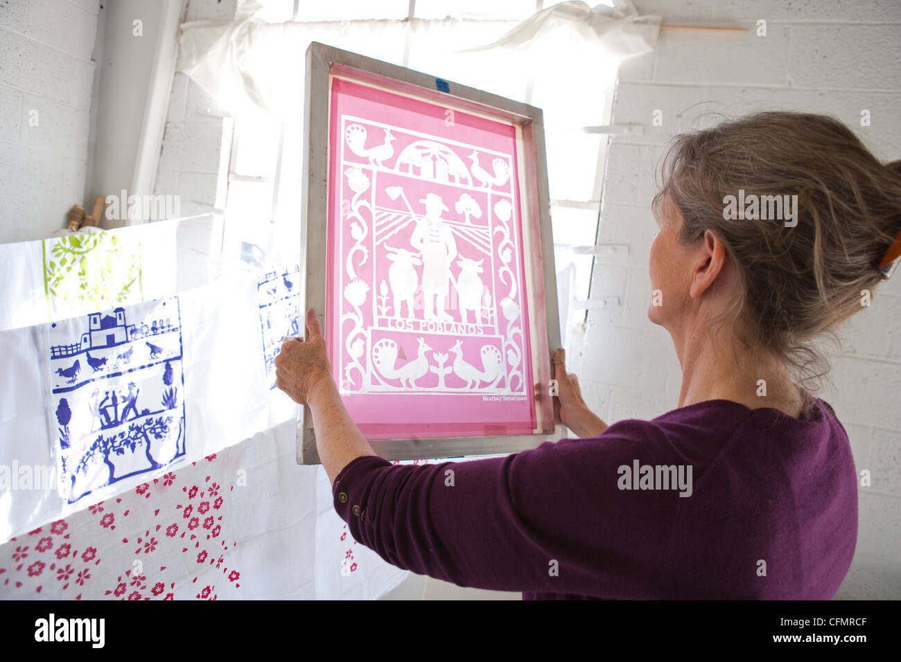 Woman in a studio holding up her silkscreen screen with light shining through. Stock Photo