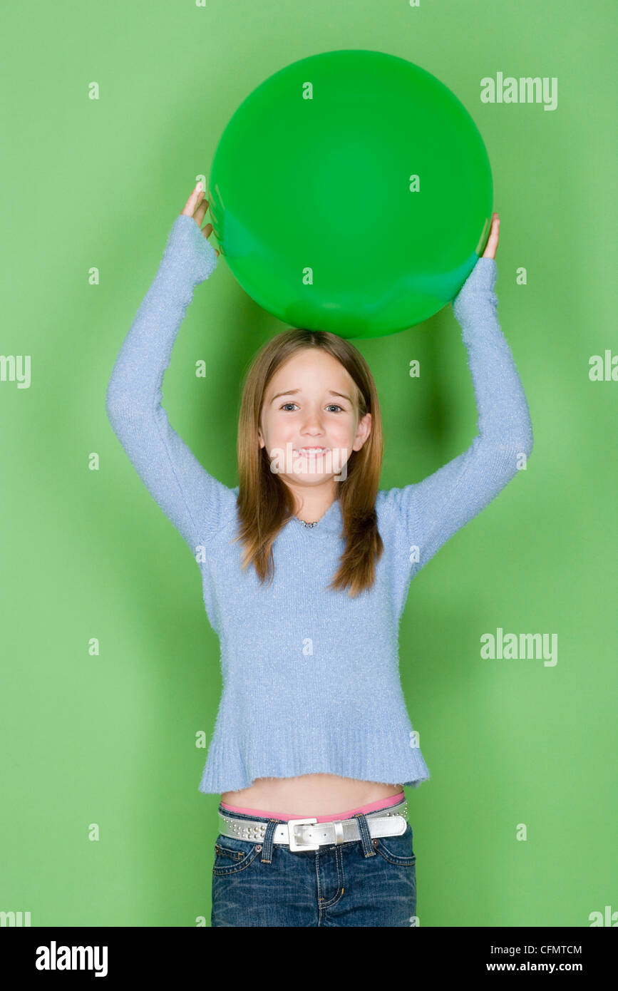 Studio shot portrait of teenage girl holding ball on her head, waist up Stock Photo