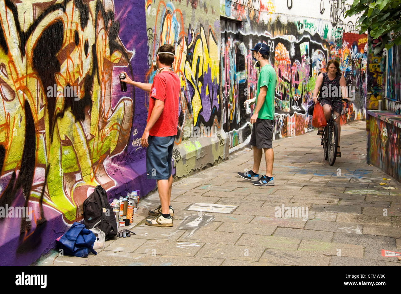 Horizontal view of Graffiti Alley Werregaran Straat in Ghent, with two artists spray painting their art onto the walkway wall. Stock Photo