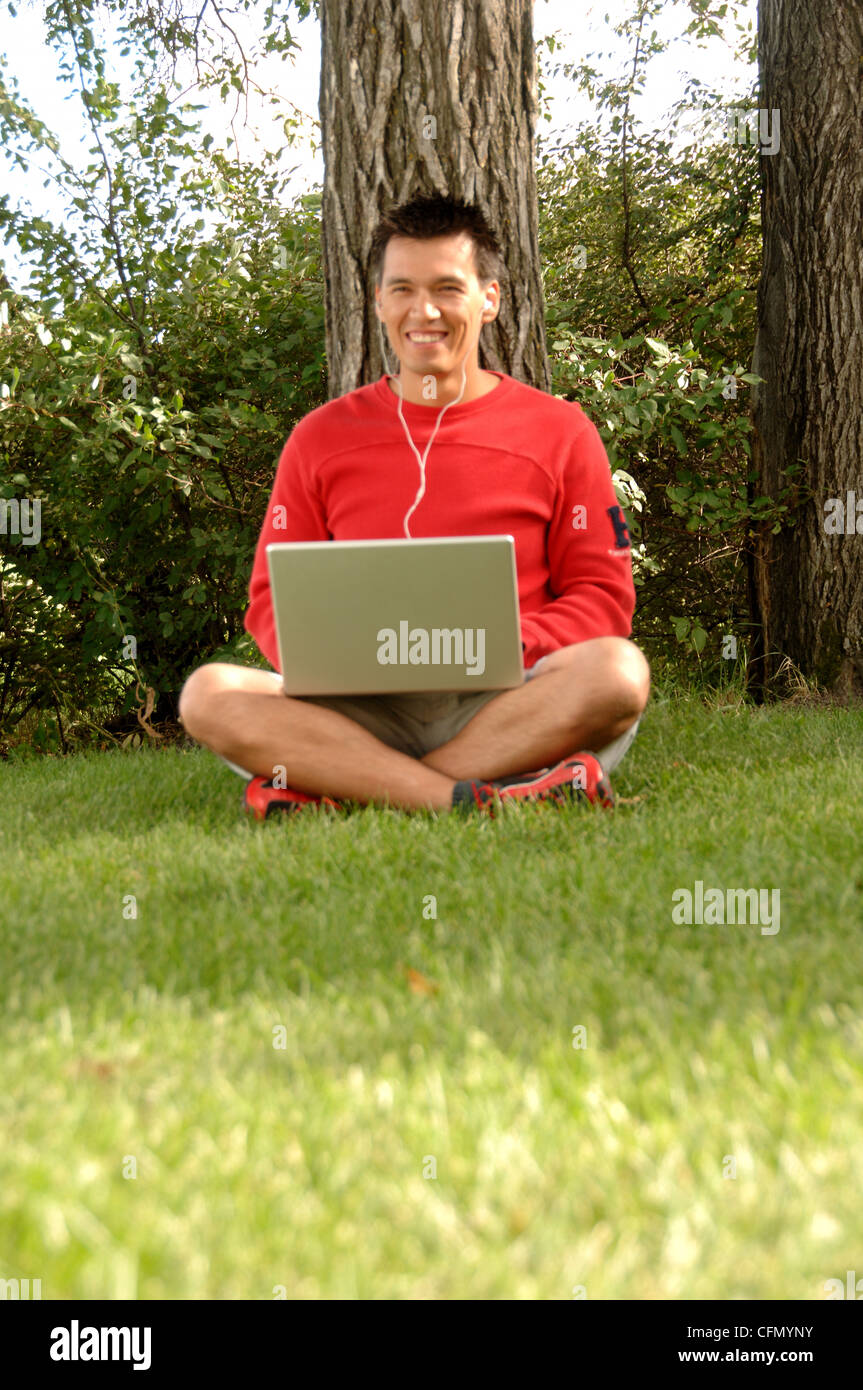 Man Sitting on Grass with Laptop and Headset Stock Photo