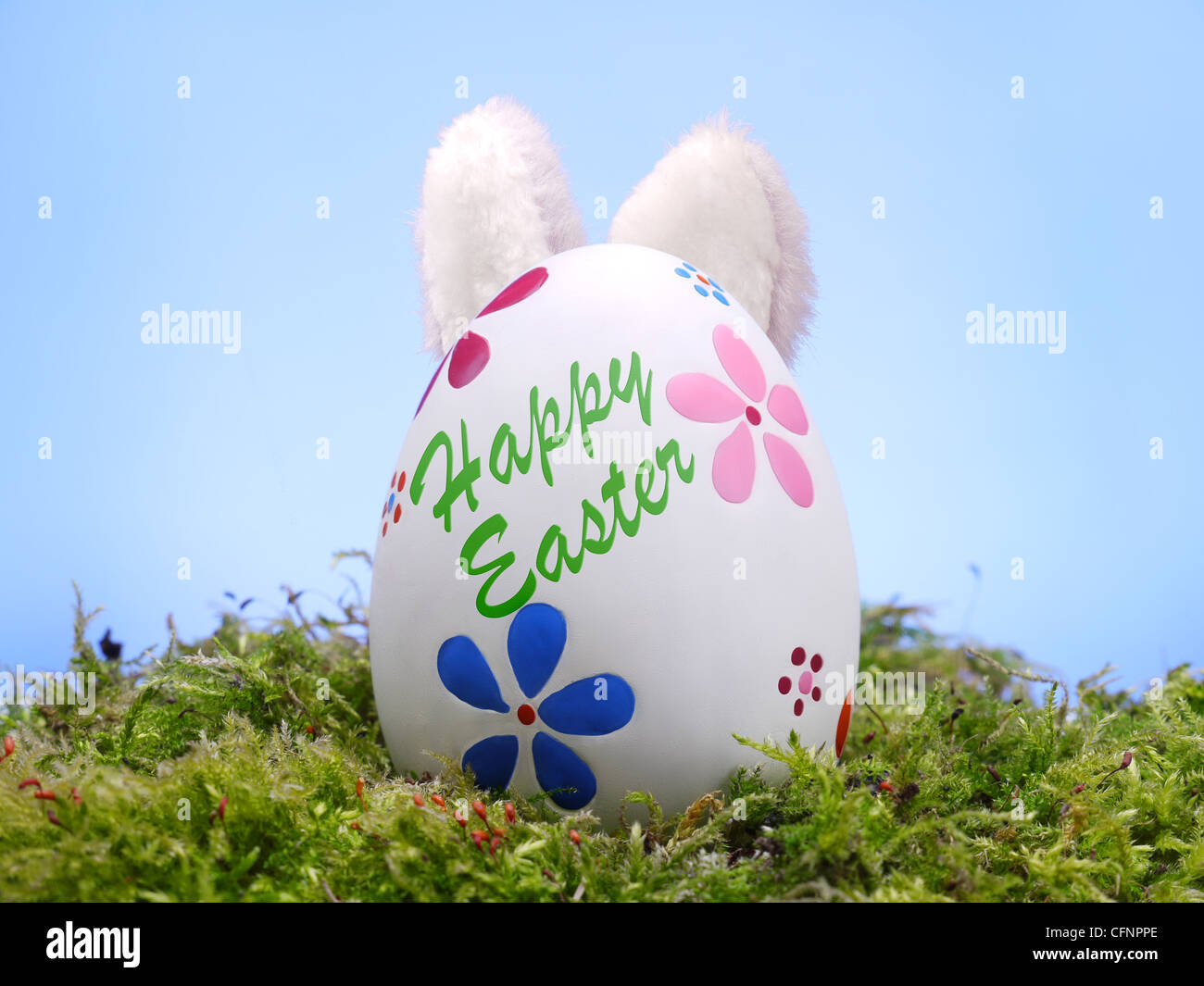 Easter egg in grass with bunny' ears poking out from behind over blue sky Stock Photo