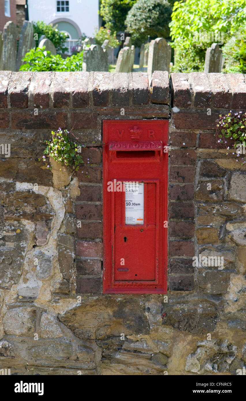 Red post box built in to a stone wall bordering a graveyard in Rye Stock Photo
