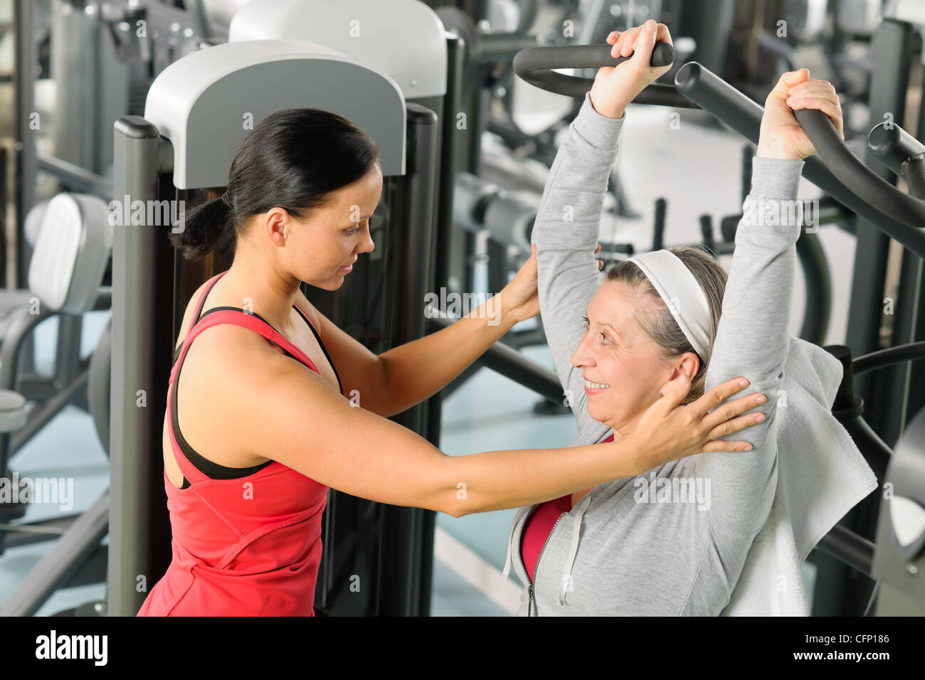 Senior woman exercise on shoulder press machine with personal trainer Stock Photo