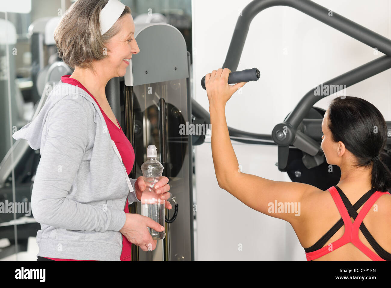 Personal trainer at fitness center showing exercise to senior woman Stock Photo