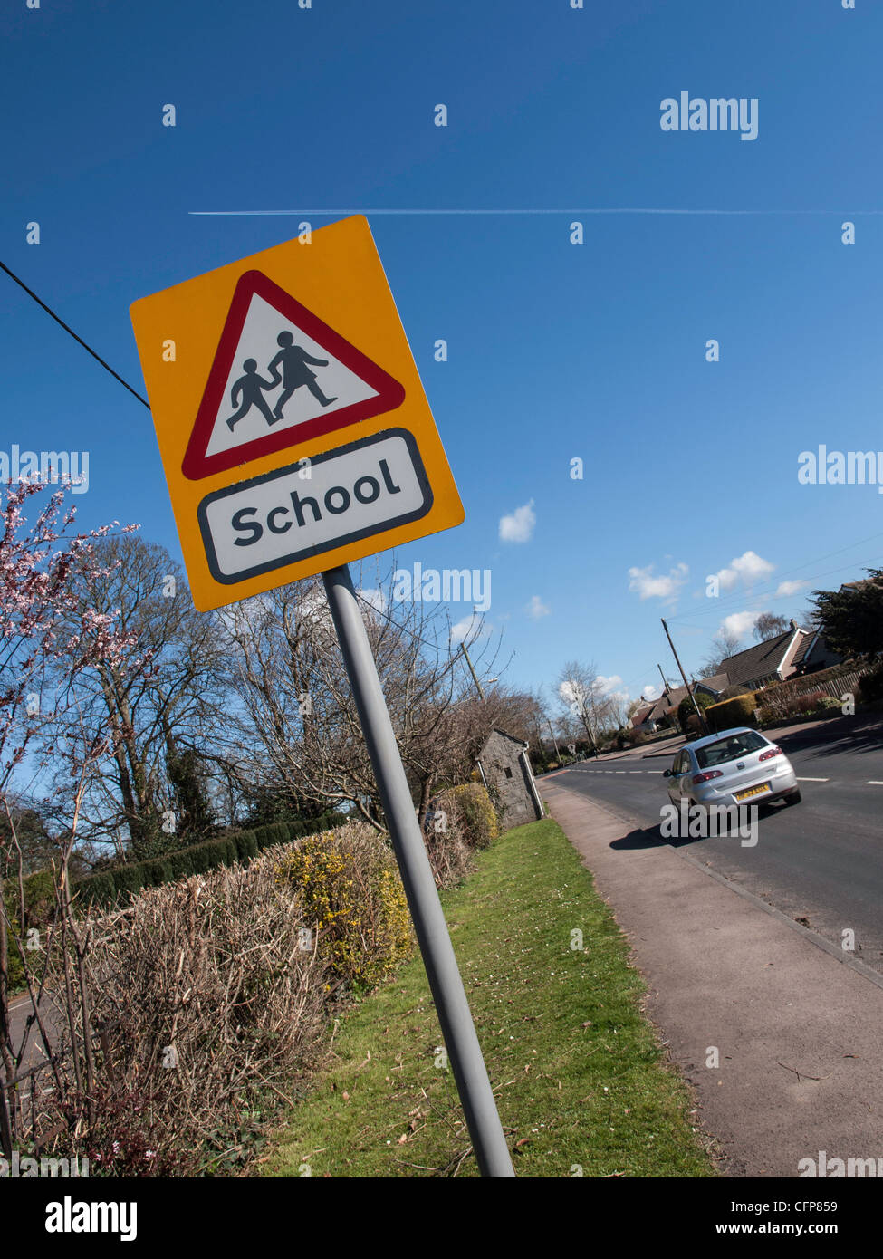 Sign warning of school ahead on country road in Gloucestershire England UK with car on road. Stock Photo