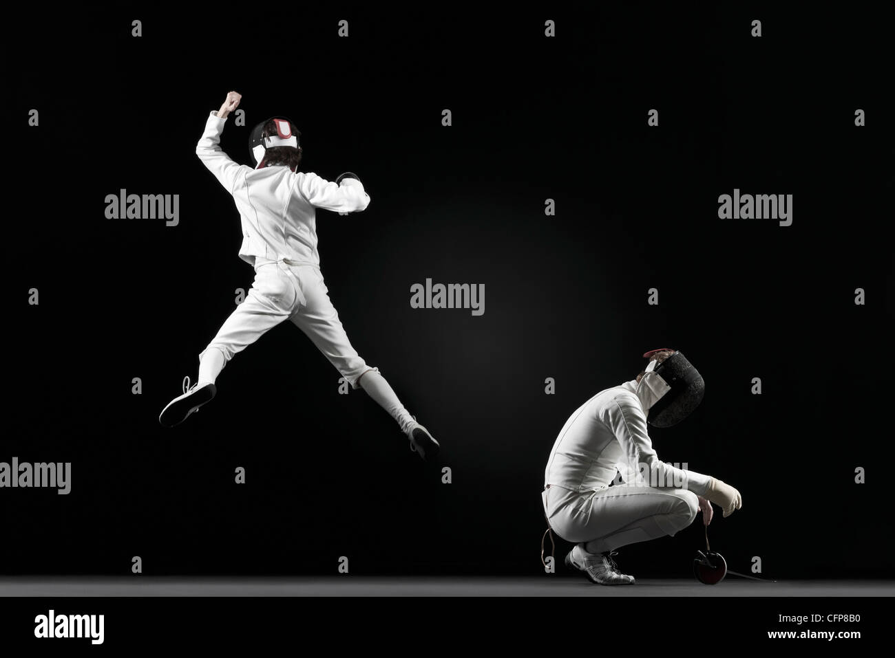 Successful fencer jumping in air next to defeated fencer Stock Photo