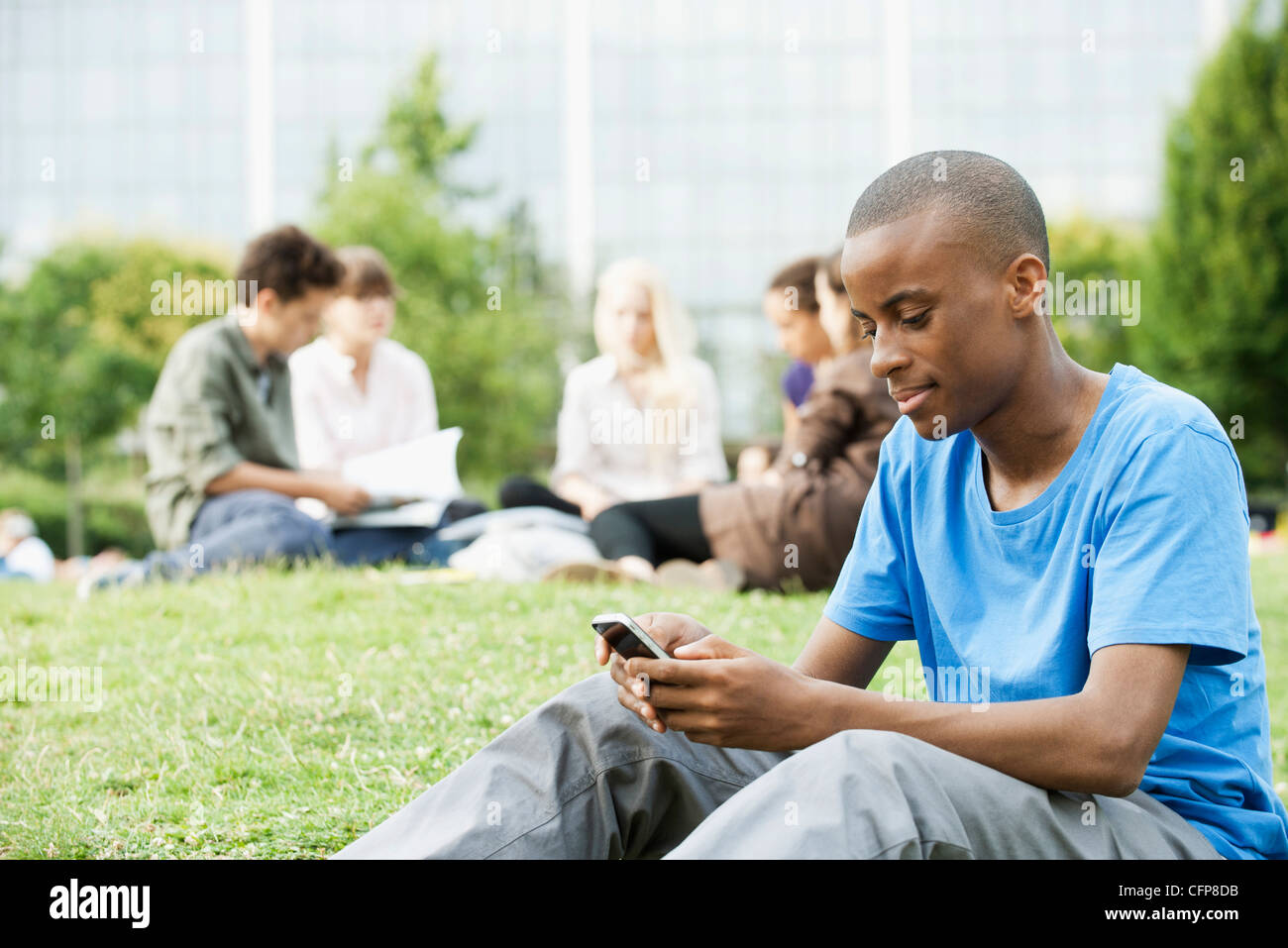 Young man text messaging with cell phone, people in background Stock Photo