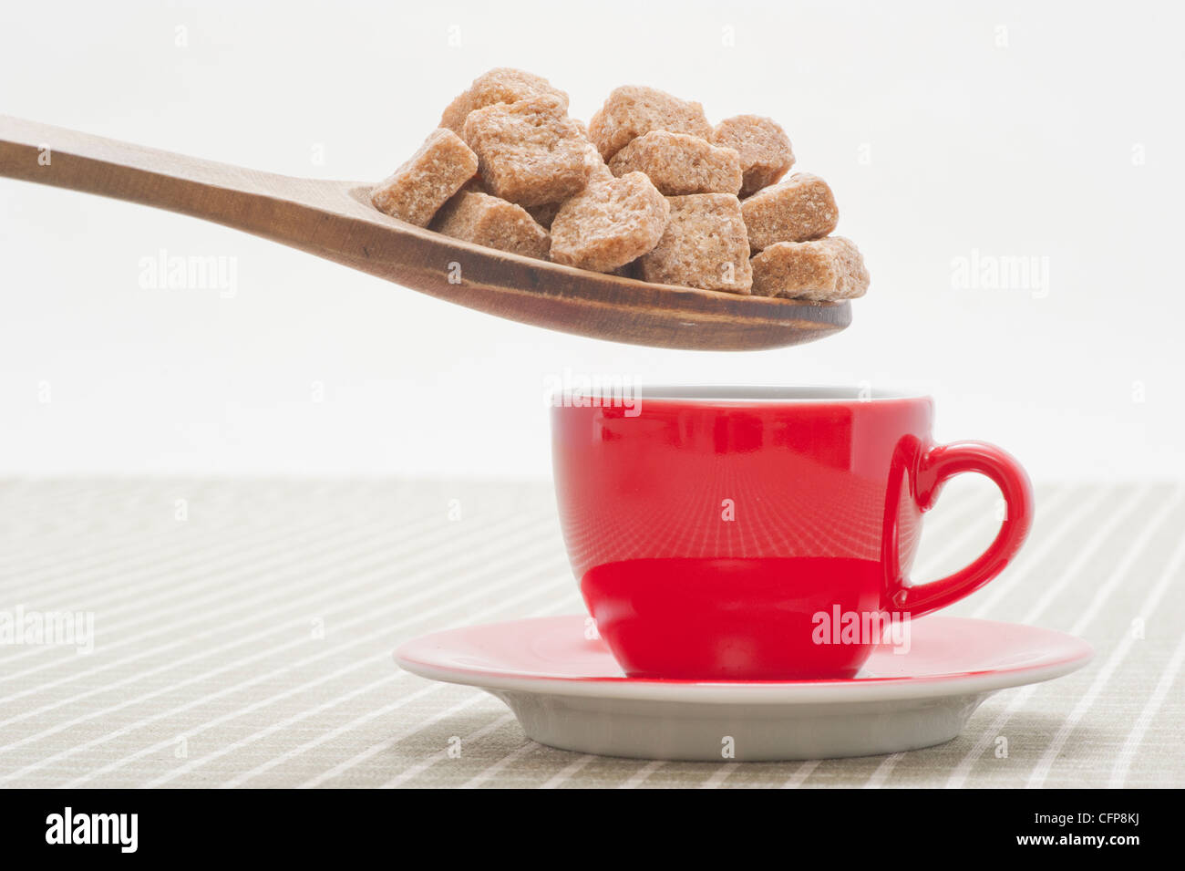 Excessive amount of brown sugar cubes being put in a red coffee cup Stock Photo