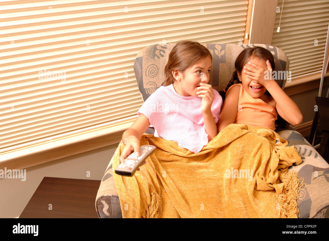 Laughing Girls Sharing Chair and Blanket Stock Photo