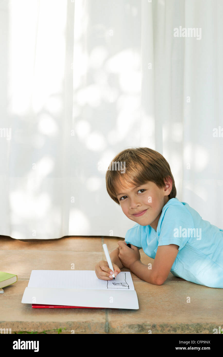 Boy lying on ground, drawing in notebook Stock Photo