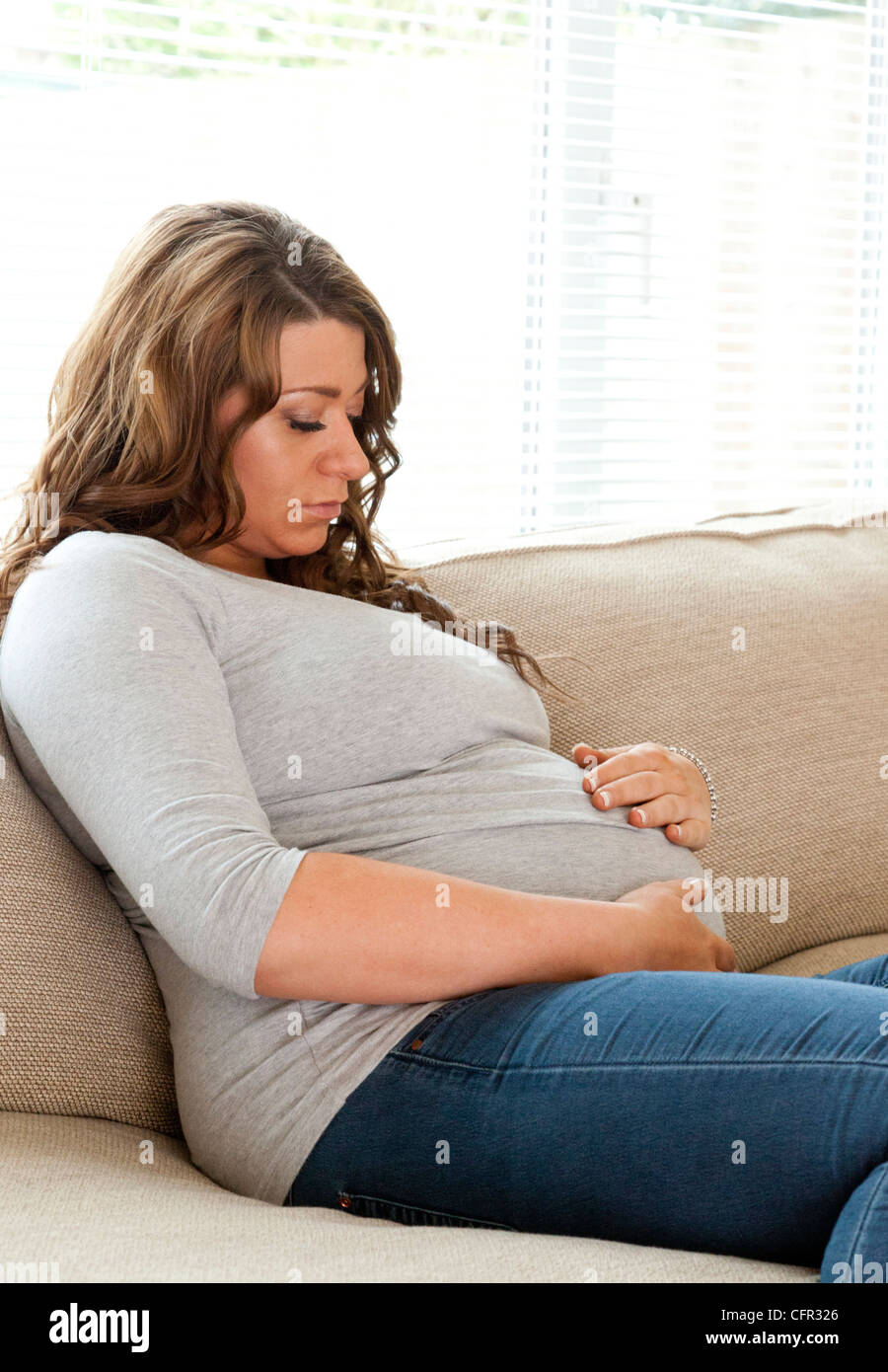 pregnant woman sat on sofa Stock Photo