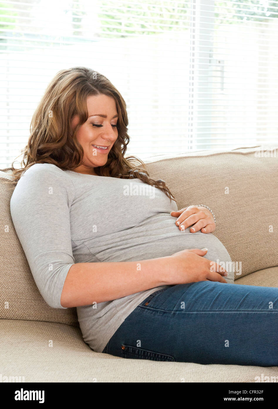 pregnant woman sat on sofa Stock Photo