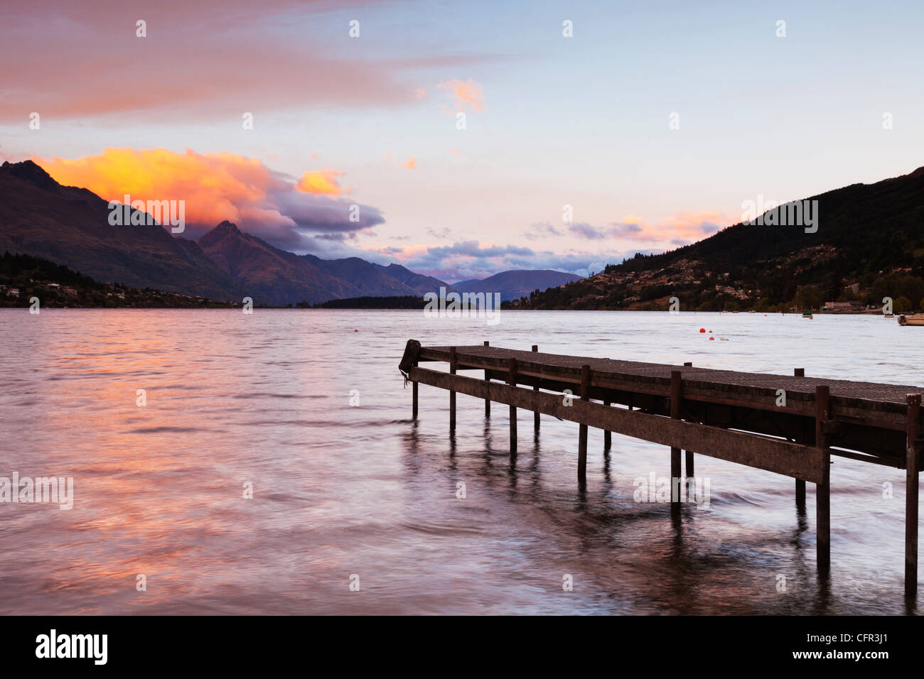 An old jetty on the shores of Lake Wakatipu, Queenstown, Otago, New Zealand, and Queenstown in the distance. Stock Photo