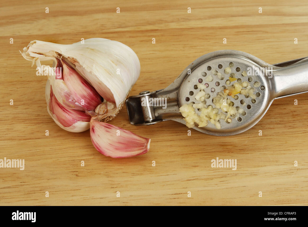 Closeup of a garlic press, a garlic bulb and cloves on a wooden board Stock Photo