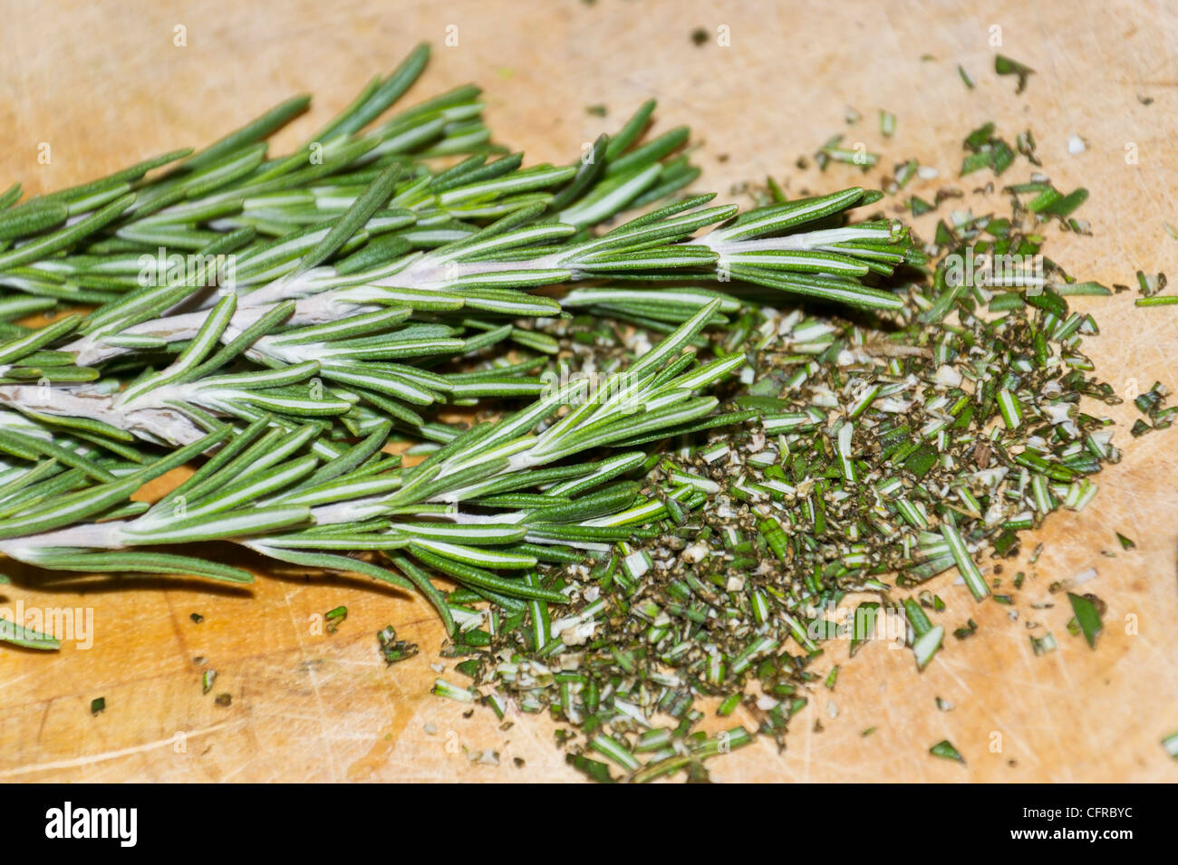 Freshly chopped sprig of rosemary herb (Rosmarinus officinalis) on a wooden cutting board. Stock Photo