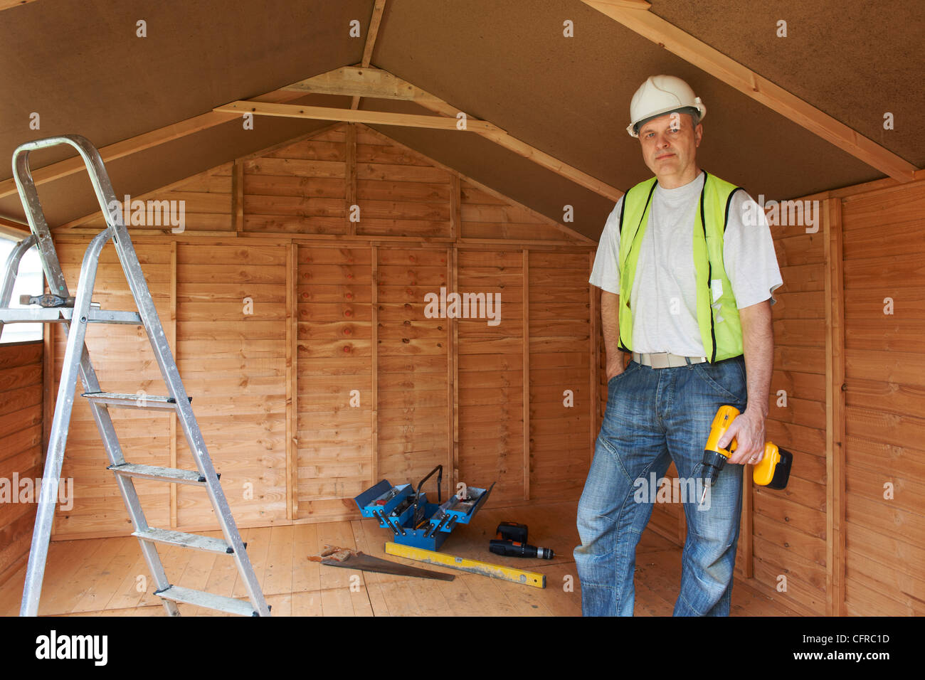 Portrait of builder standing by ladder with hard hat and high visibility jacket Stock Photo