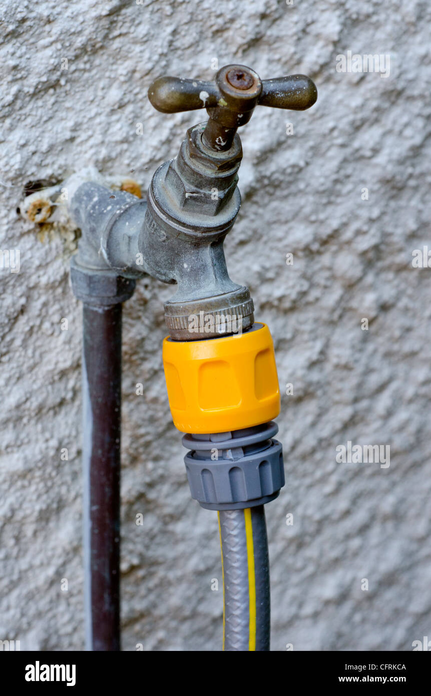 Outdoor garden water tap with hose pipe connected. Stock Photo