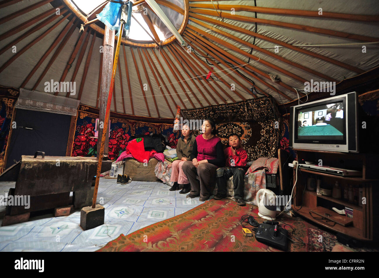 Mongolia, Baganuur, family in casual dress, sitting on sofa in yurt by television and looking away Stock Photo