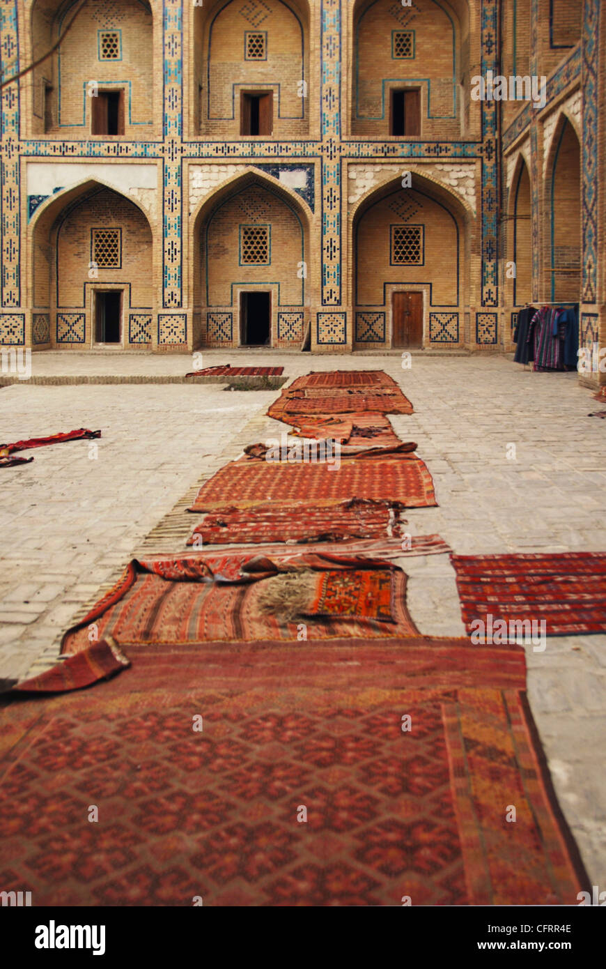 Uzbekistan, Bukhara, arched entrance in a row of historic building with carpets lying on courtyard Stock Photo