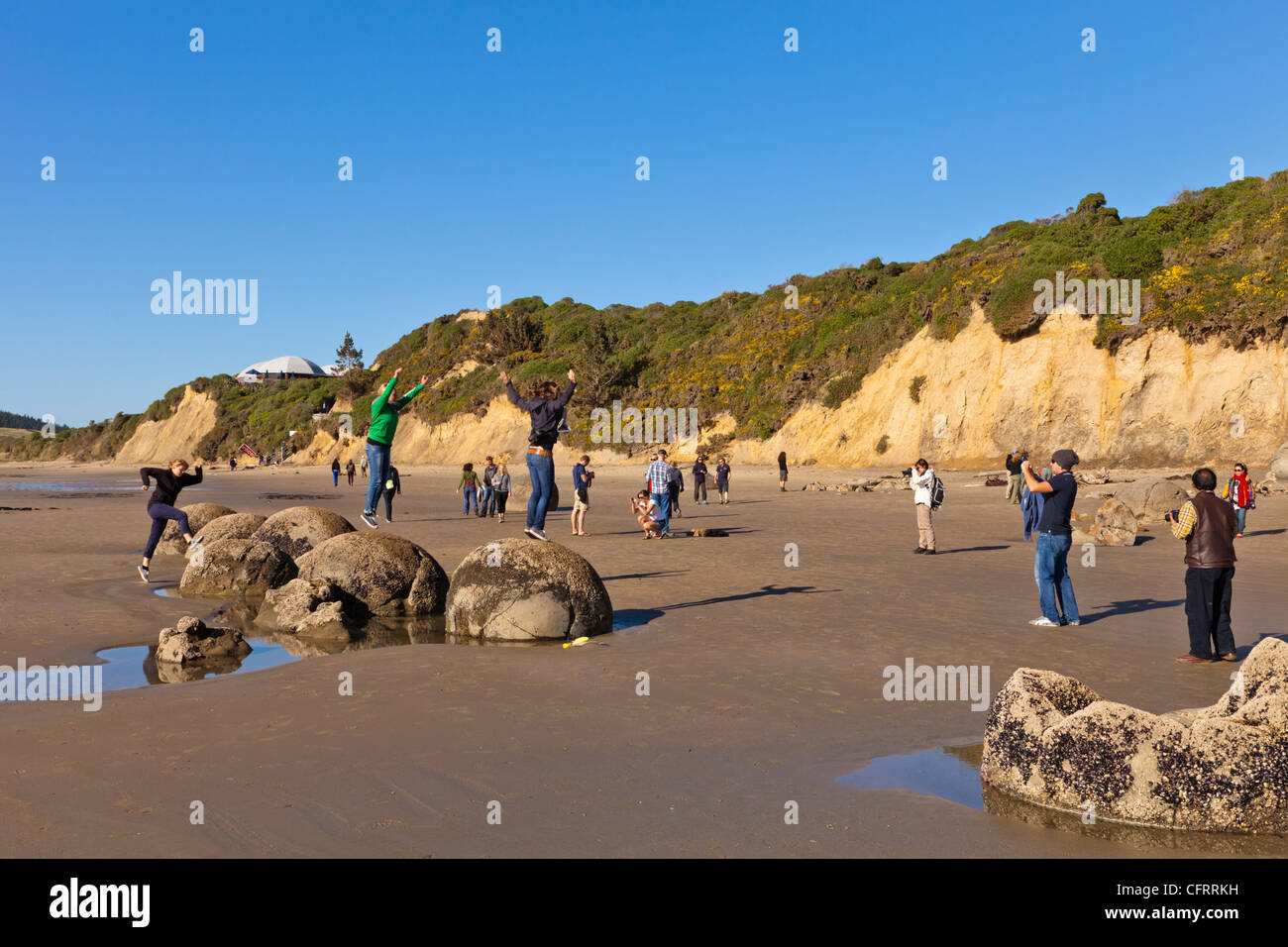 Tourists posing and taking photos at Moeraki Boulders at low tide, Otago, New Zealand. Stock Photo