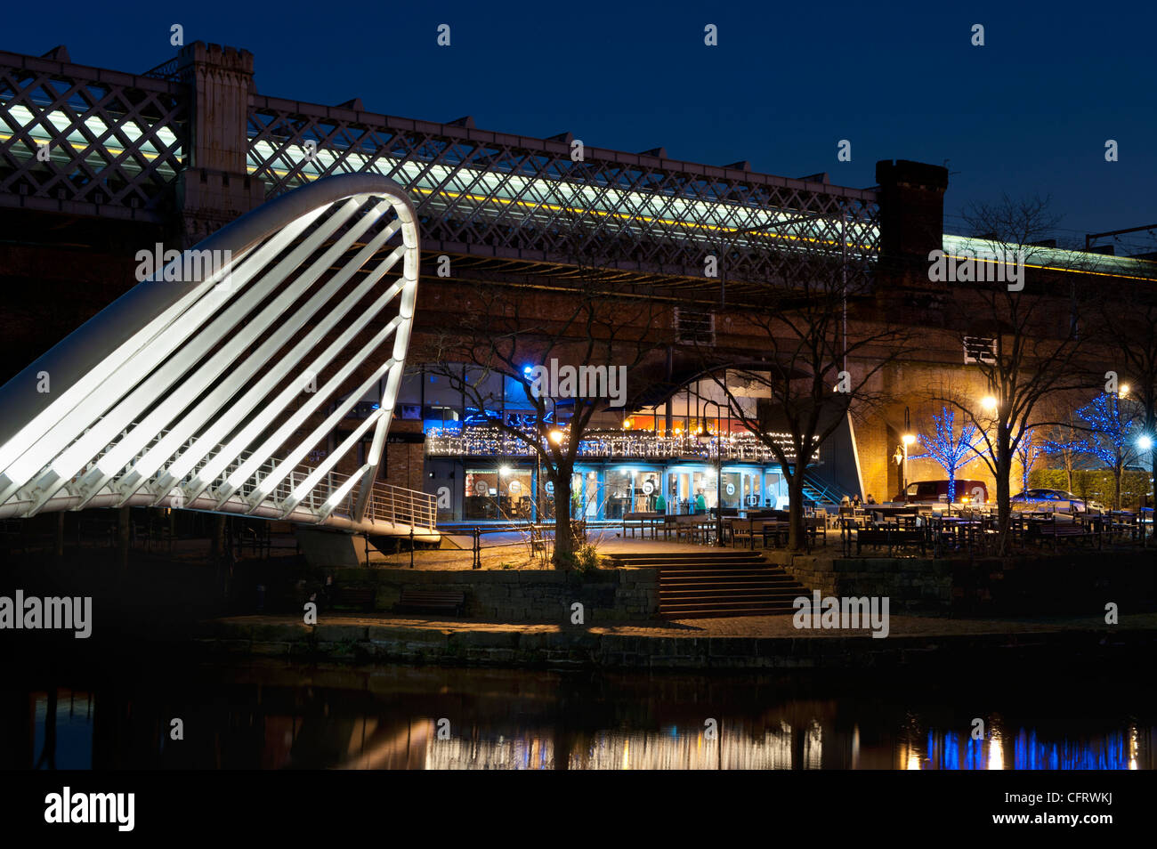 A night shot of canal at Castlefield, as a train rushes past over a bridge in the background. Stock Photo