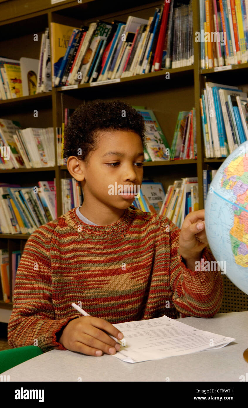 Eleven Year Old Boy Pointing to Globe in School Library Stock Photo