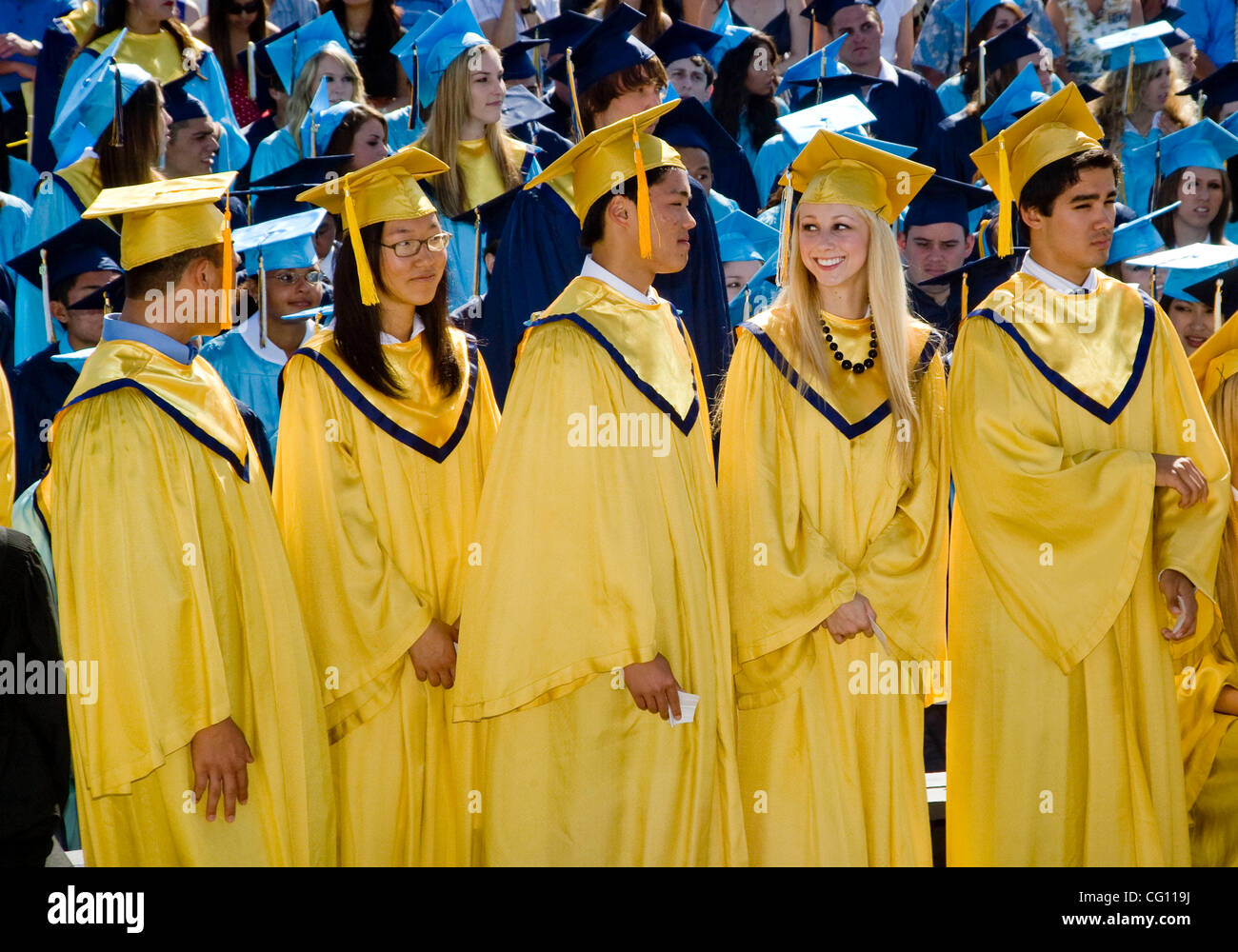 Wearing caps and gowns, high school seniors participate in graduation exercises in Huntington Beach, CA. The yellow gowns denote academic elite students with a 4.0 or higher grade index. Stock Photo