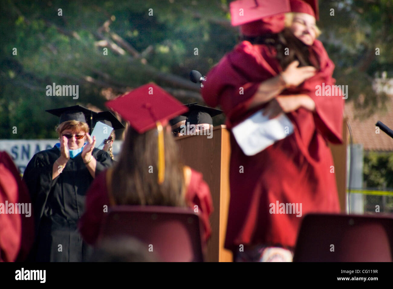 Wearing caps and gowns, two high school senior class speakers hug at