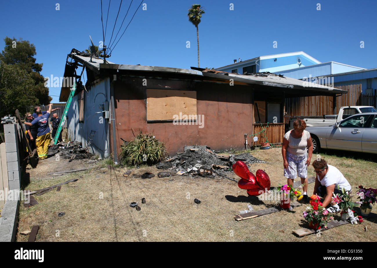 As firefighters survey the scene, (L-R) Luz M. Quintana, from San Pablo, and her sister Guadalupe Rojas, from Modesto, drop off flowers at a makeshift memorial in front of the Moore residence on Sunday, July 22, 2007 in the Montalvin Manor Neighborhood in unincorporated San Pablo, Calif. Yesterday,  Stock Photo