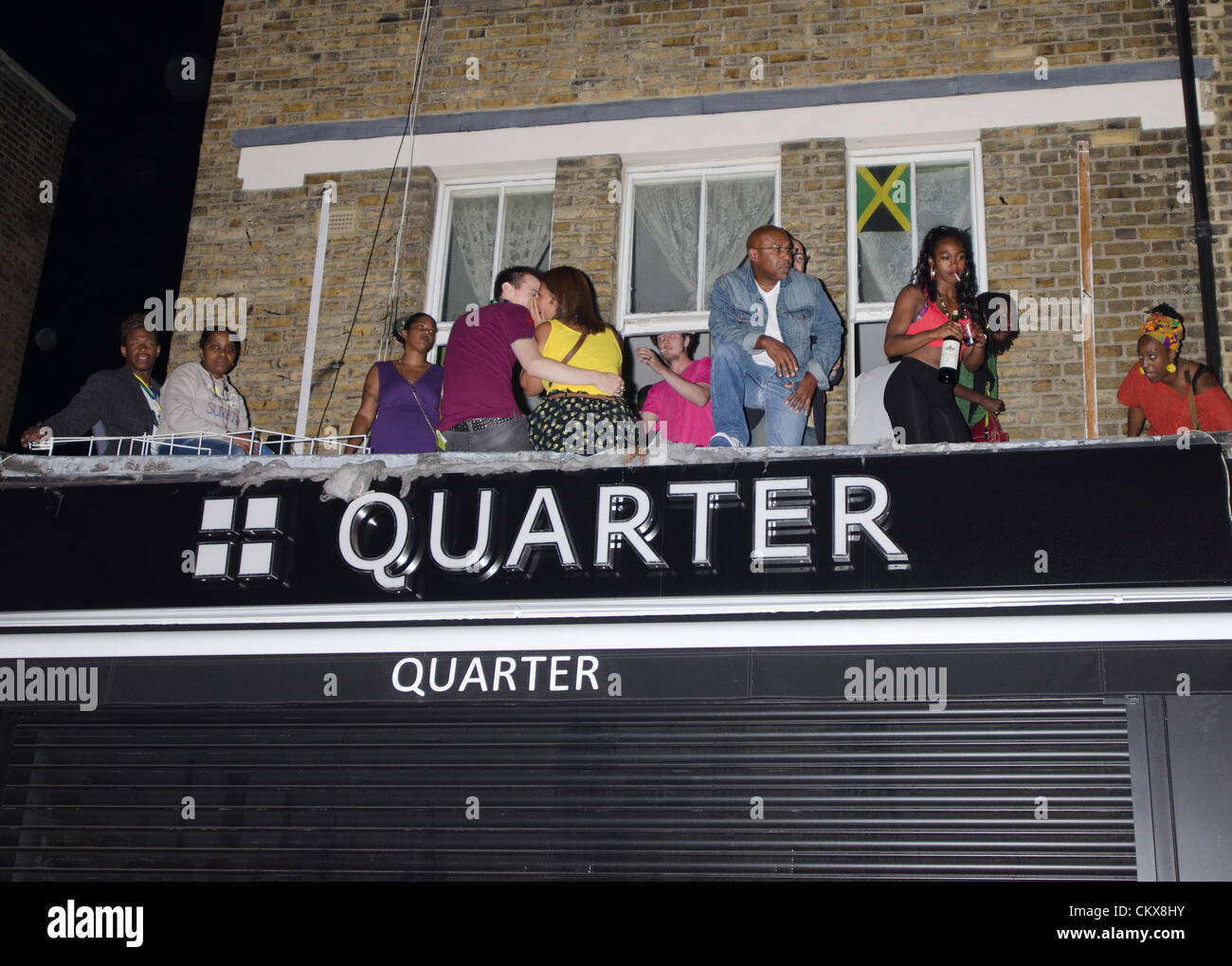 revellers party on balcony above shop Notting Hill Carnival street at night London Uk Quarter Stock Photo