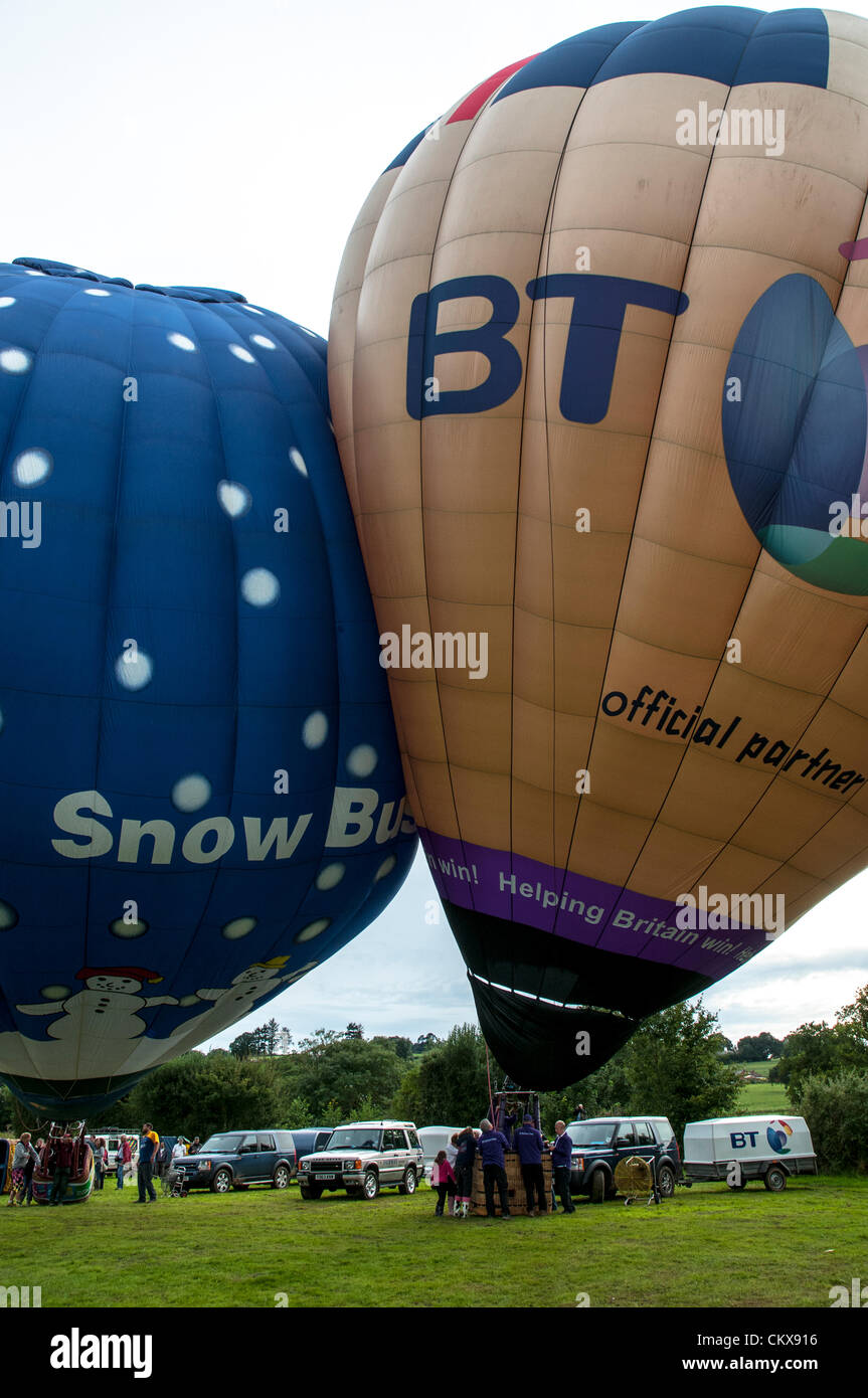 26th Aug 2012. Dave Baker G-ZOIZ M-Type (M-105) BT LONDON 2012 balloon and the G-SBIZ Cameron Z.90 Snow Business Hot Air Free Balloon bump together as they prepare for launch at the Tiverton balloon festival in Tiverton, Devon, UK. Stock Photo