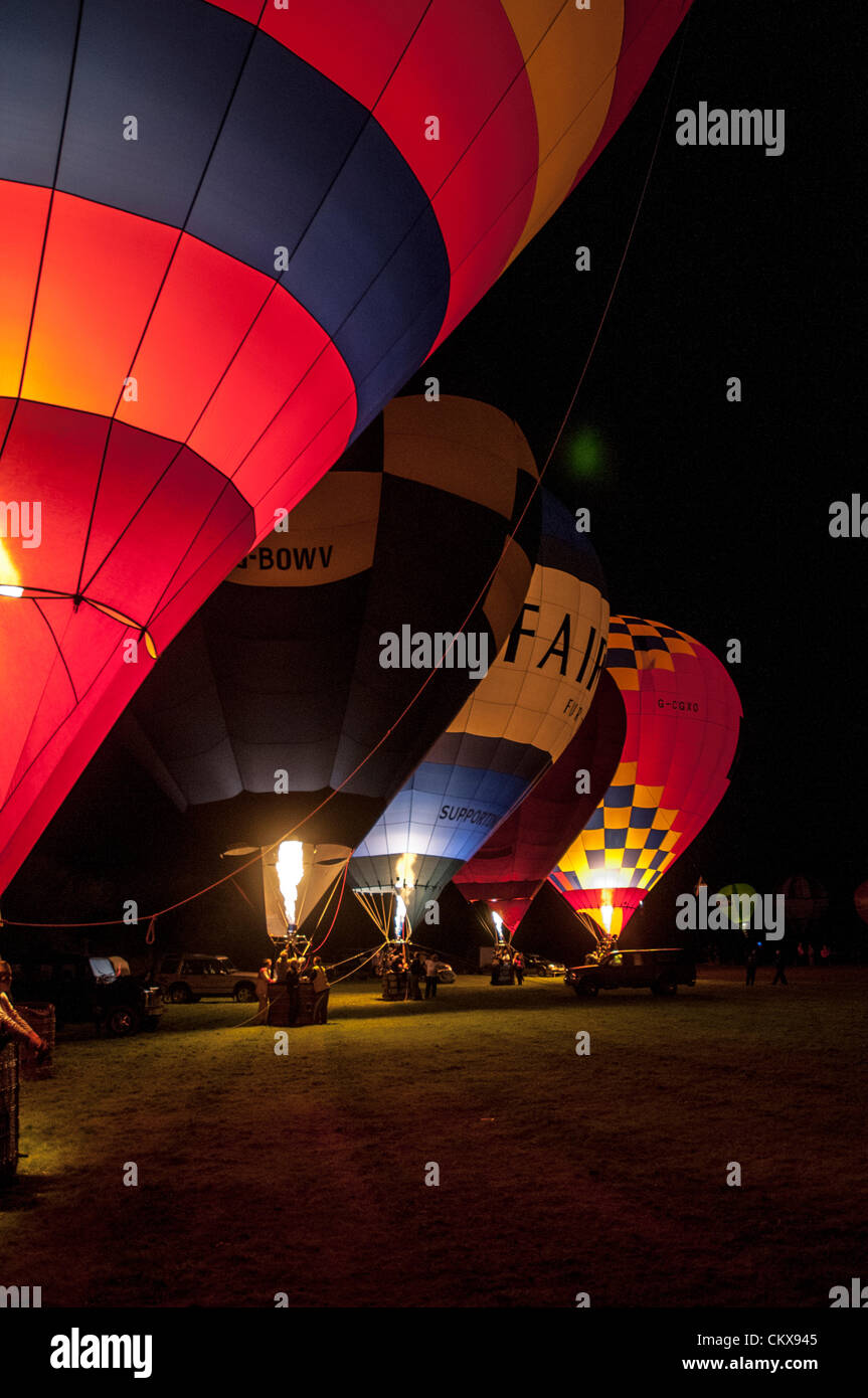 26th Aug 2012. The John Harris (G-CDWD) University of Bristol balloon,the Robert Harris G-BOWV Cameron V-65 balloon, the Peter harding LINDSTRAND 90A Fairway Furniture balloon, the CAMERON V-56 G-BFFT balloon and the Charlie Street Lindstrand LBL-105A, G-CGXO, Aerosaurus Balloon light-up during the nightglow at the Tiverton Balloon festival, Devon, UK. Stock Photo