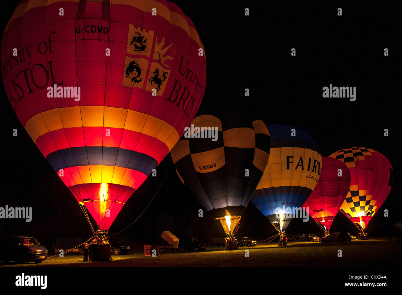 26th Aug 2012. The John Harris (G-CDWD) University of Bristol balloon,the Robert Harris G-BOWV Cameron V-65 balloon, the Peter harding LINDSTRAND 90A Fairway Furniture balloon, the CAMERON V-56 G-BFFT balloon and the Charlie Street Lindstrand LBL-105A, G-CGXO, Aerosaurus Balloon light-up during the nightglow at the Tiverton Balloon festival, Devon, UK. Stock Photo