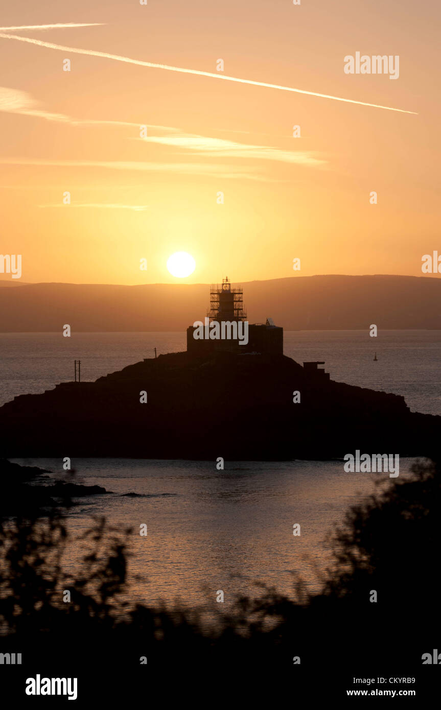 5th September 2012 - Swansea - UK :  The sun rises over Mumbles lighthouse (built in 1794)  in Swansea Bay this morning on the start of a warm Autumn day. The 115 foot high lighthouse is in the process of being repainted by it's owners Trinity House - hence the scaffolding around the 200 year old structure. Stock Photo