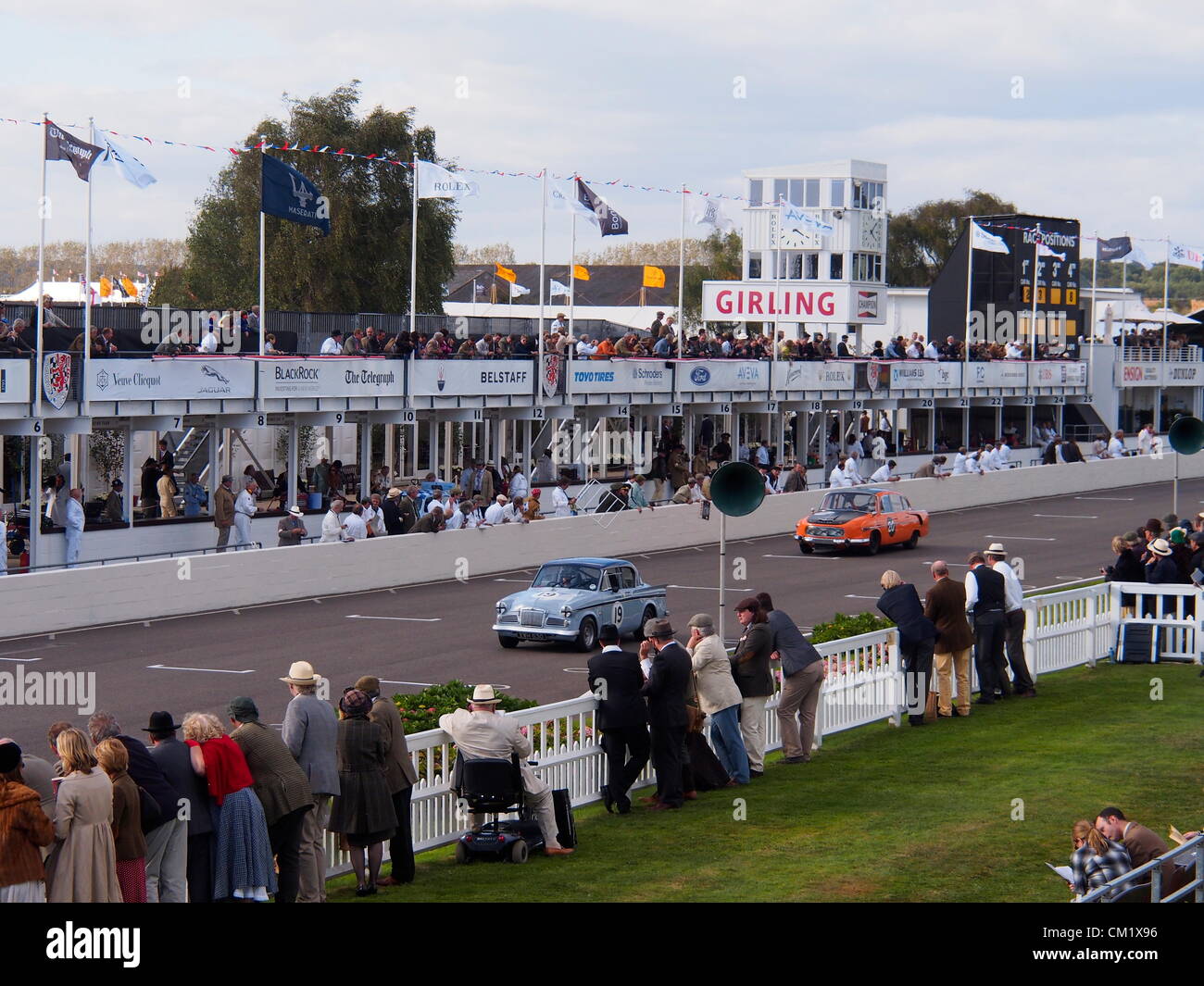 Goodwood Revival Practice Day Friday September 14th.2012. A racing Tatra in bright orange livery and carrying the number 20, and a Sunbeam Rapier carrying the number 19,approach the finish line in front of the pits and watching crowds at this historic venue. Stock Photo