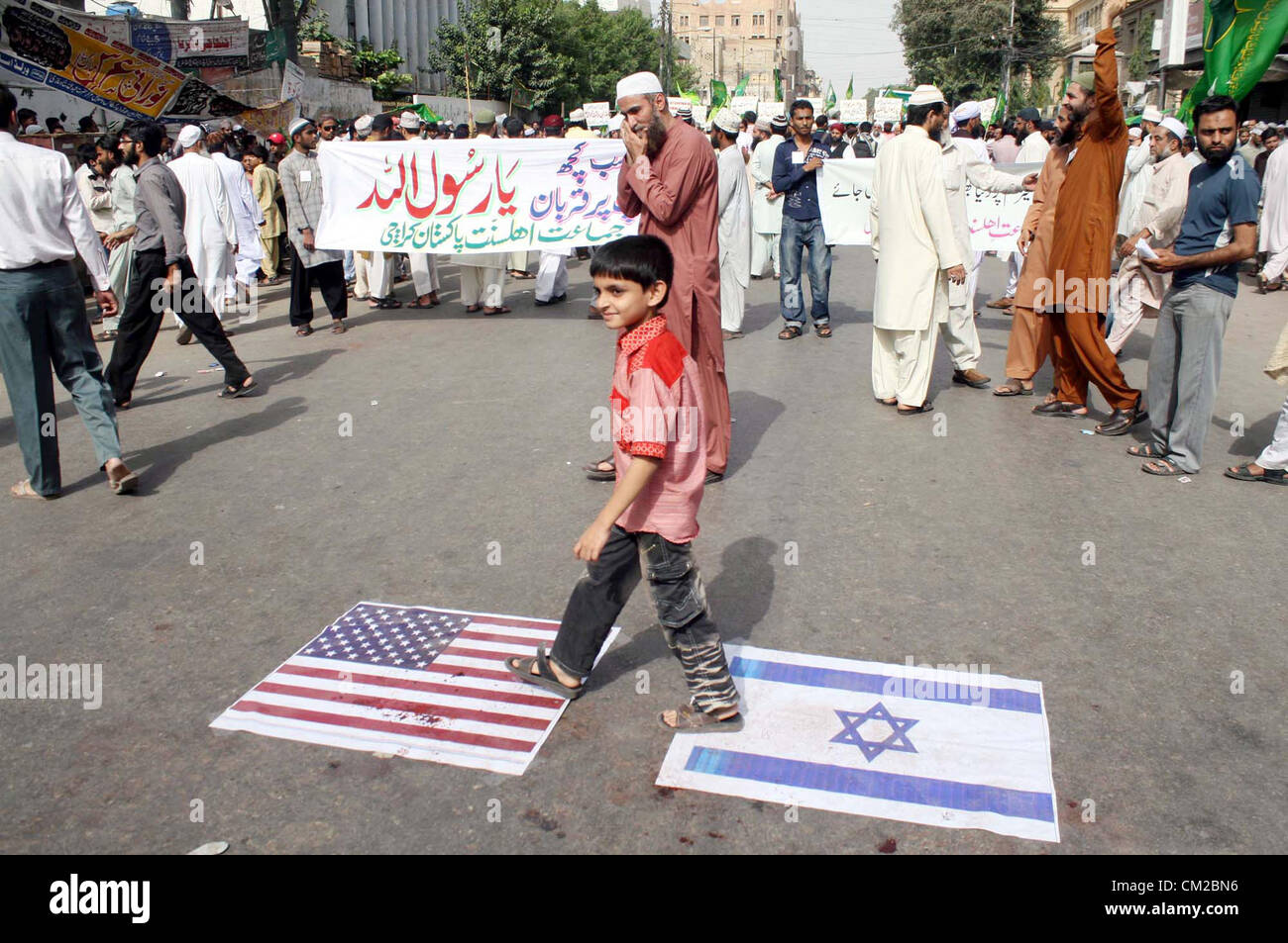 A child walks on US and Israel flag during a protest rally  against blasphemy anti-Islamic movie released on the Internet by USA, organized by Jamat-e- Ahle Sunnat at MA Jinnah Road in Karachi on Wednesday, September 19, 2012. Stock Photo