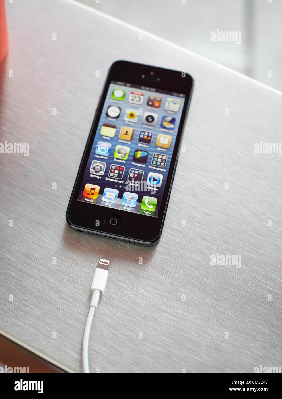 Inside a coffee shop, a newly released, black, Apple iPhone 5 sits face up on a metal countertop next to Apple's Lightning Connection cable. The iPhone 5 became available to public on Friday, September 21, 2012. Stock Photo