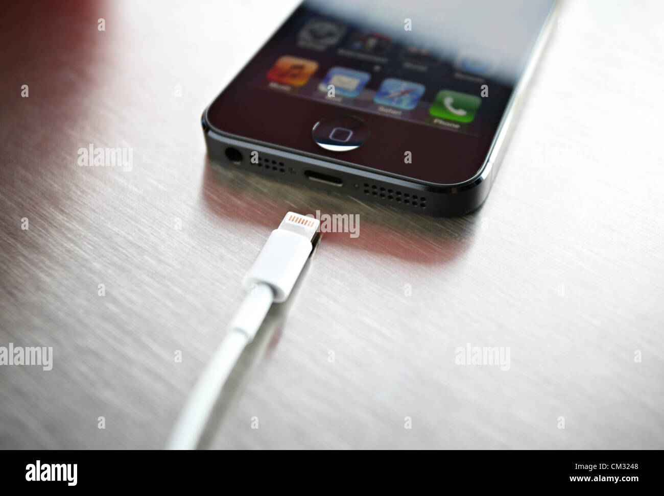 Inside a coffee shop, a newly released, black, Apple iPhone 5 sits face up on a metal countertop next to Apple's Lightning Connection cable. The iPhone 5 became available to public on Friday, September 21, 2012. Stock Photo