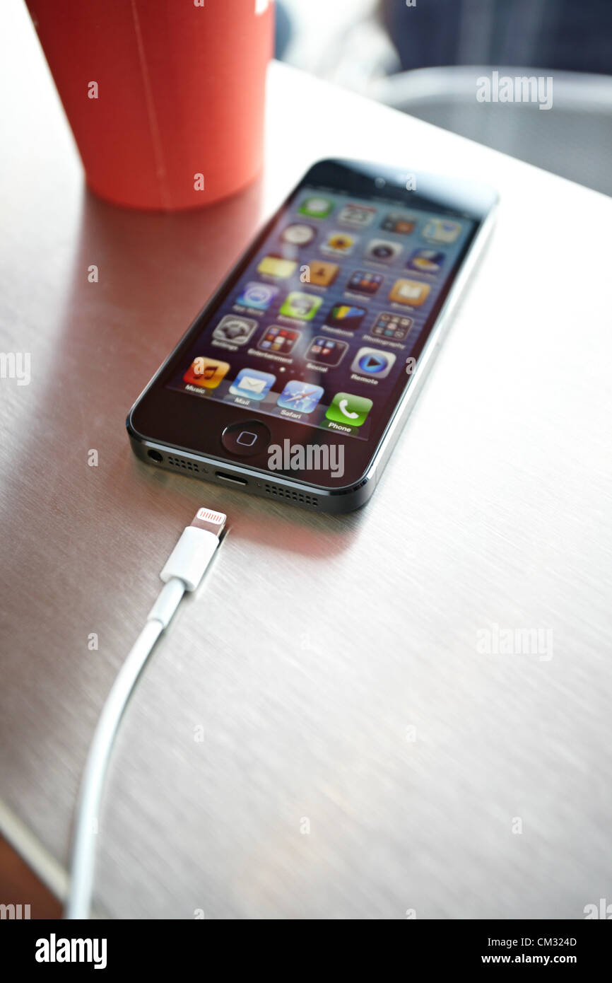 Inside a coffee shop, a newly released, black, Apple iPhone 5 sits face up on a metal countertop next to Apple's Lightning Connection cable. The iPhone 5 became available to public on Friday, September 21, 2012. Stock Photo