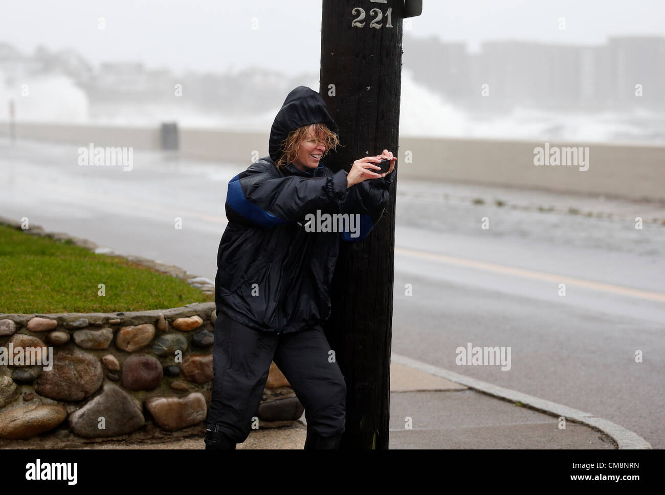 Winthrop, Massachusetts, USA. A woman braces herself against the wind from Hurricane Sandy as she photographs the waves coming ashore in Winthrop, Massachusetts, Monday, Oct. 29, 2012. The huge weather system  is predicted  to make landfall in southern New Jersey late Monday and is affecting weather up and down the East Coast of the United States. Stock Photo